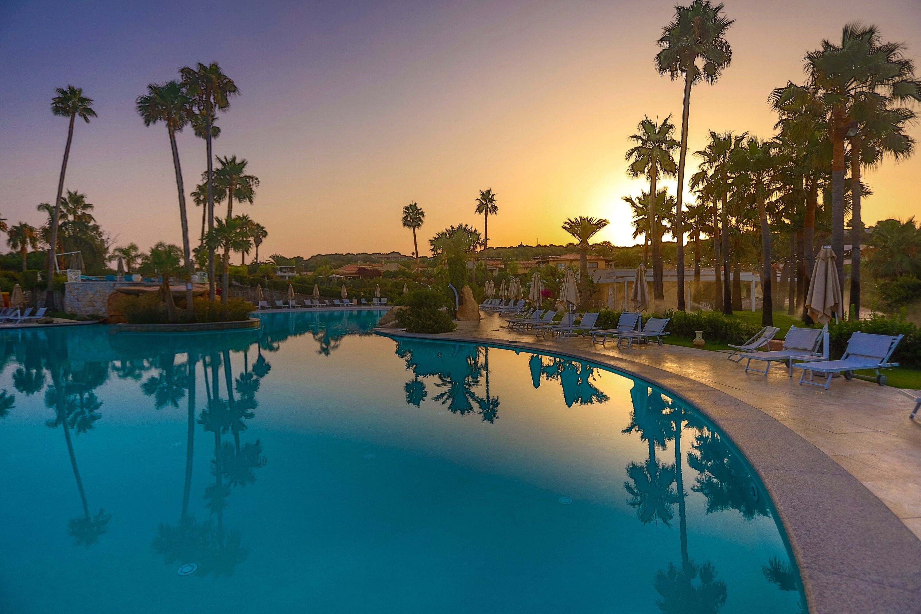 A pool with palm trees and lounge chairs, surrounded by a landscaped area.