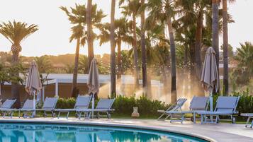 Un espace aménagé au bord de la piscine, avec des chaises longues et des parasols, entouré de palmiers.