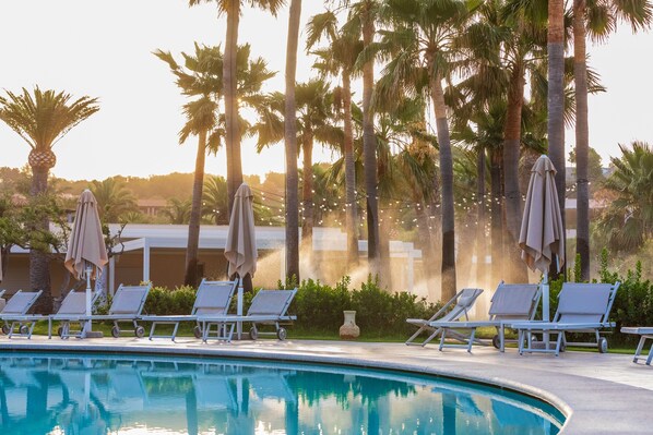 A poolside area with lounge chairs and umbrellas, surrounded by palm trees. - Hotel Club Saraceno (Tortoli)