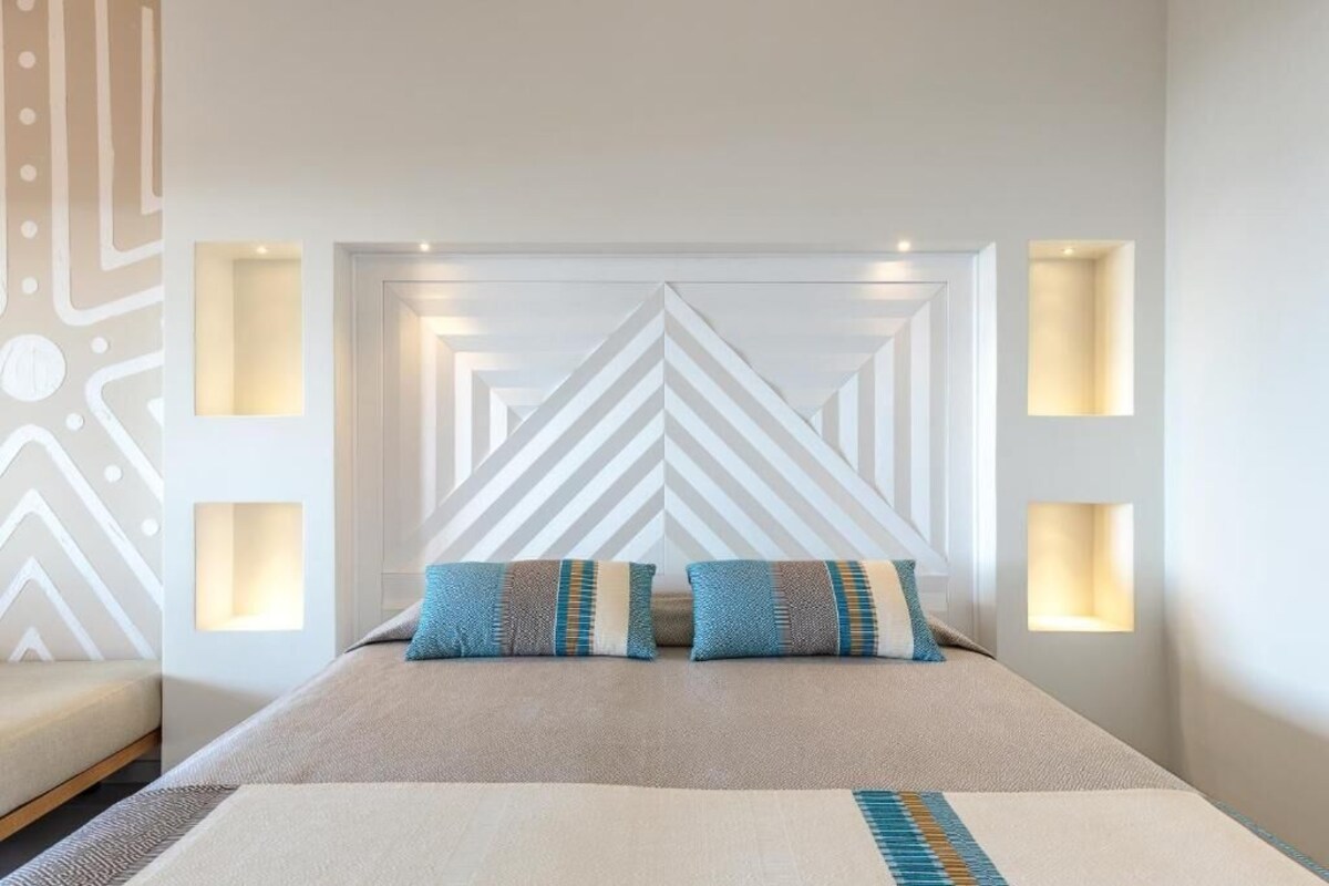 A modern hotel room with a large bed, geometric wall design, and built-in lighting.