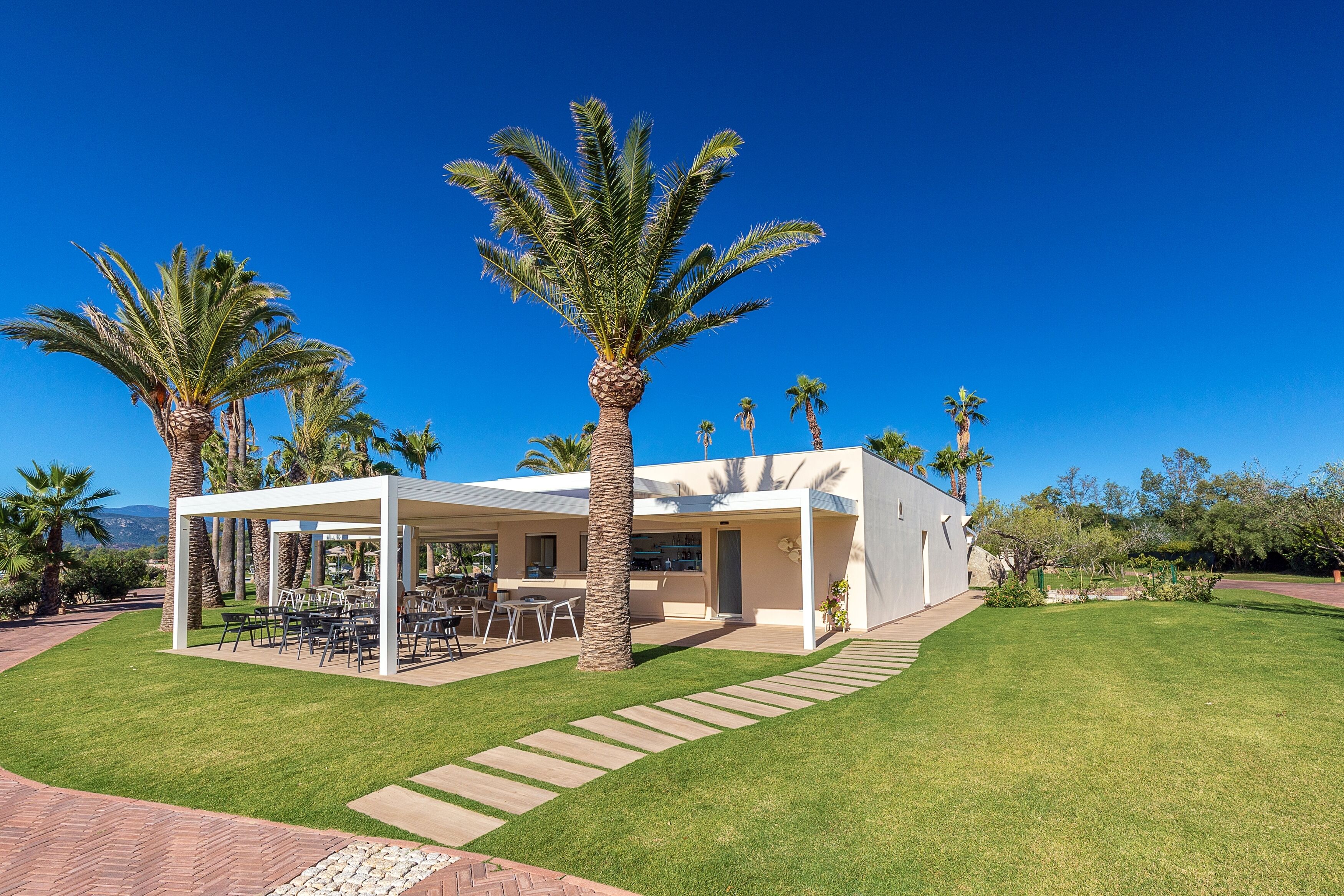A modern house with a covered patio, palm trees, and a well-maintained lawn.