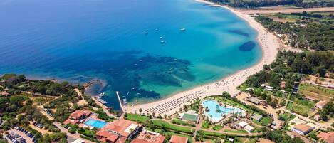 An aerial view of a coastal resort with a beach, swimming pool, and residential buildings.