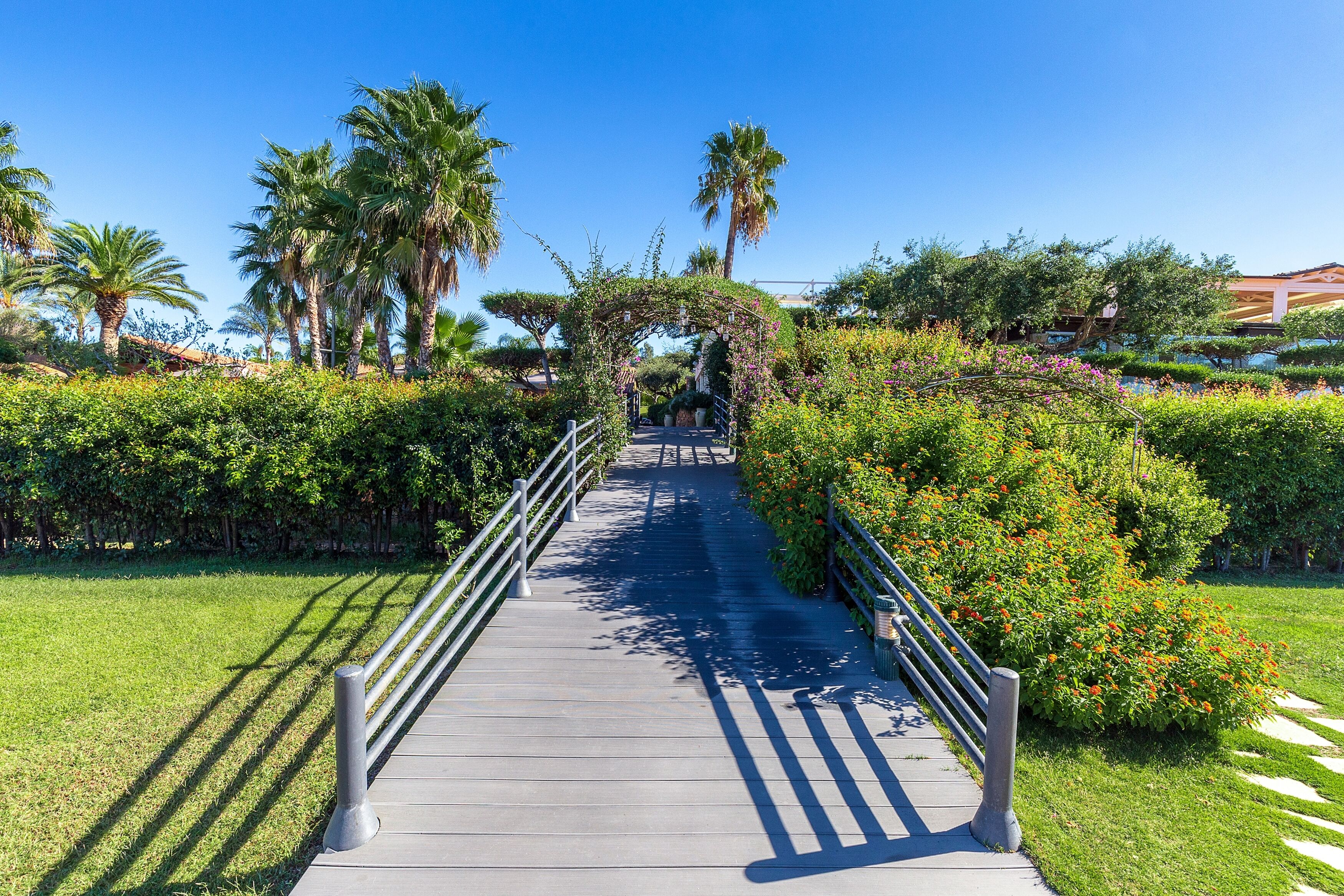 A pathway leading to a building with a covered entrance, surrounded by lush greenery and palm trees.