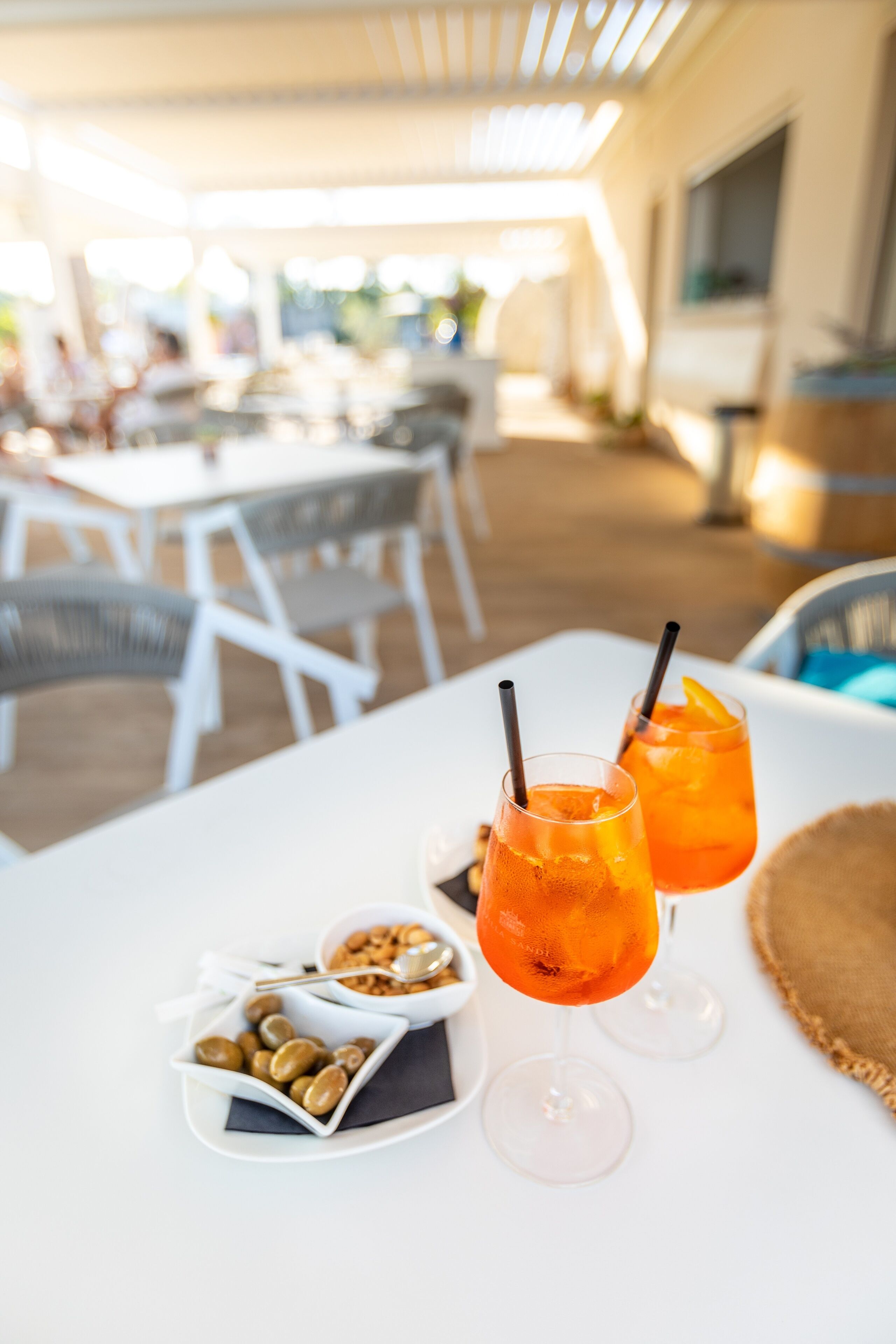 A table with two drinks, a bowl of nuts, and a plate of olives.
