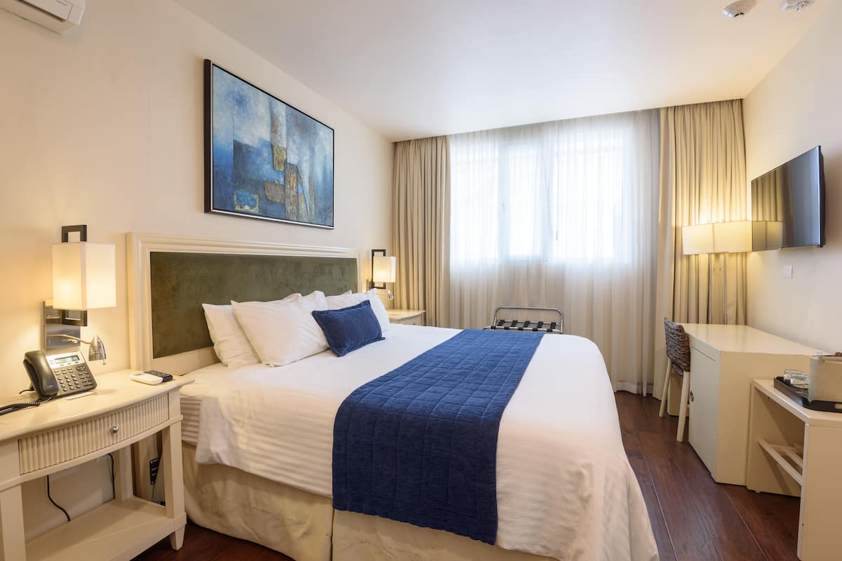 Une chambre d’hôtel avec un grand lit, un bureau, une chaise, une télévision et un tableau au mur.