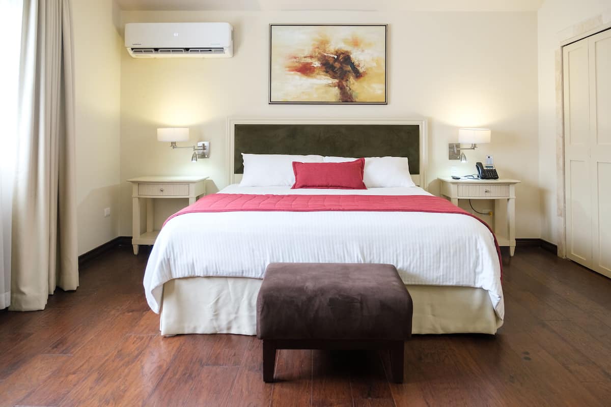 Une chambre d’hôtel avec un grand lit, une table de chevet avec une lampe, une petite table avec un téléphone et un climatiseur fixé au mur.