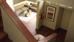 Un escalier en bois mène à un espace de vie comprenant un canapé, une table basse et un tableau accroché au mur.
