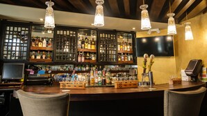 Un espace bar doté d’étagères en bois où sont exposées différentes bouteilles d’alcool, d’un comptoir et de luminaires suspendus en cristal.