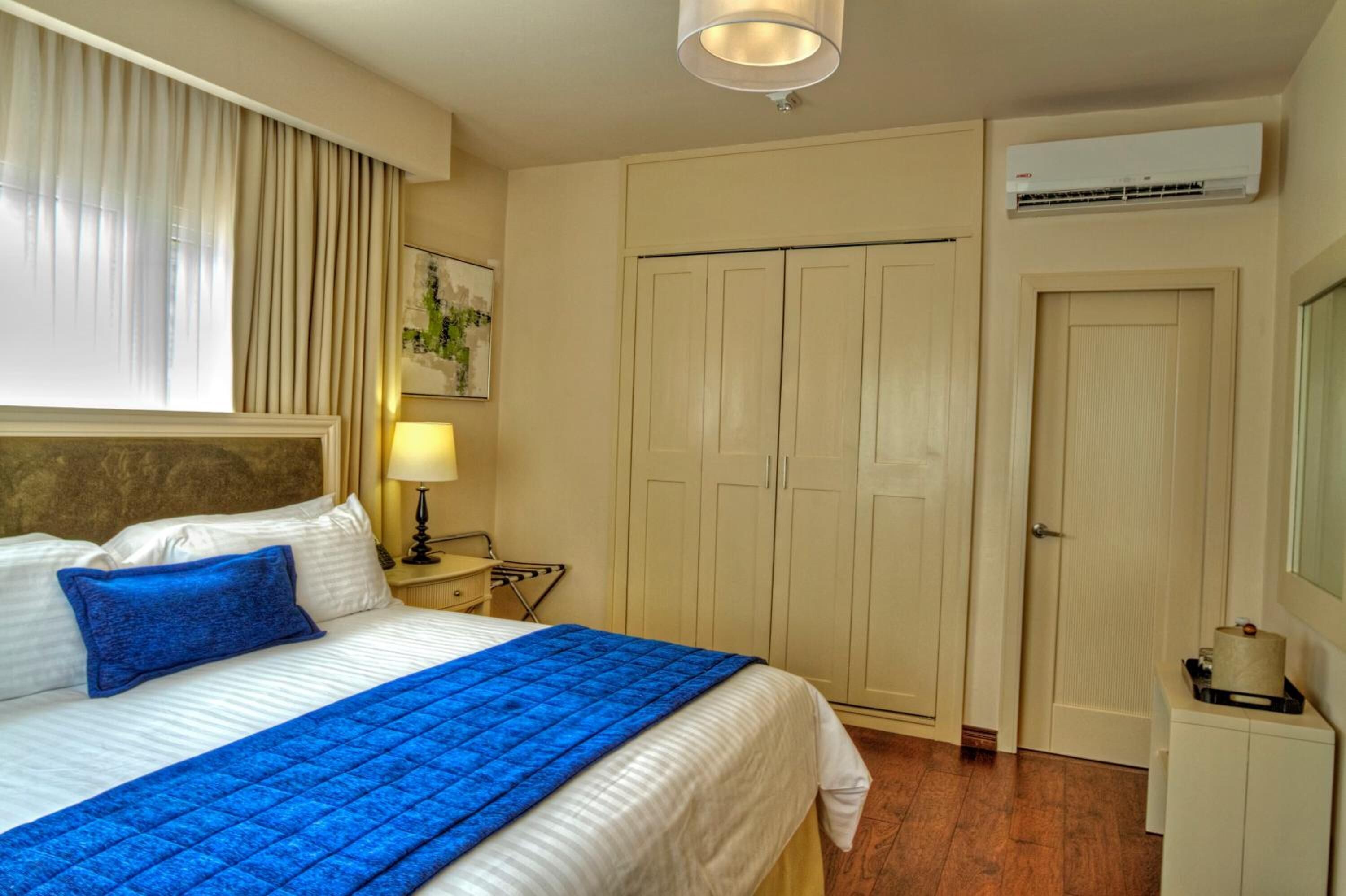 Una habitación de hotel con cama, mesita de noche, lámpara, armario y aire acondicionado.
