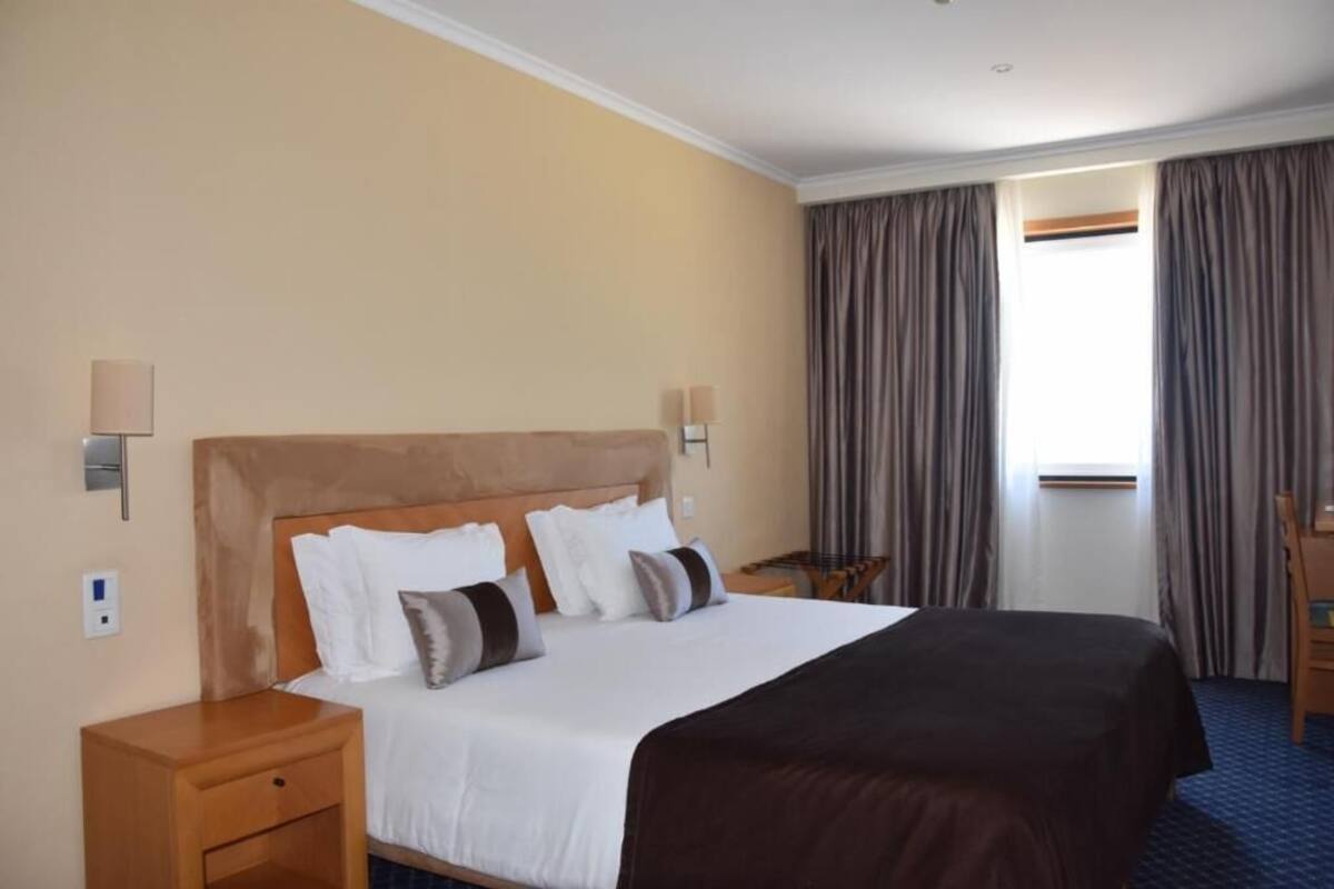 A hotel room with a large bed, two bedside tables, a nightstand, a desk, and a chair.
