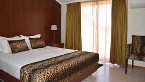 Quarto de hotel com uma cama grande, uma cadeira e uma janela com cortinas.