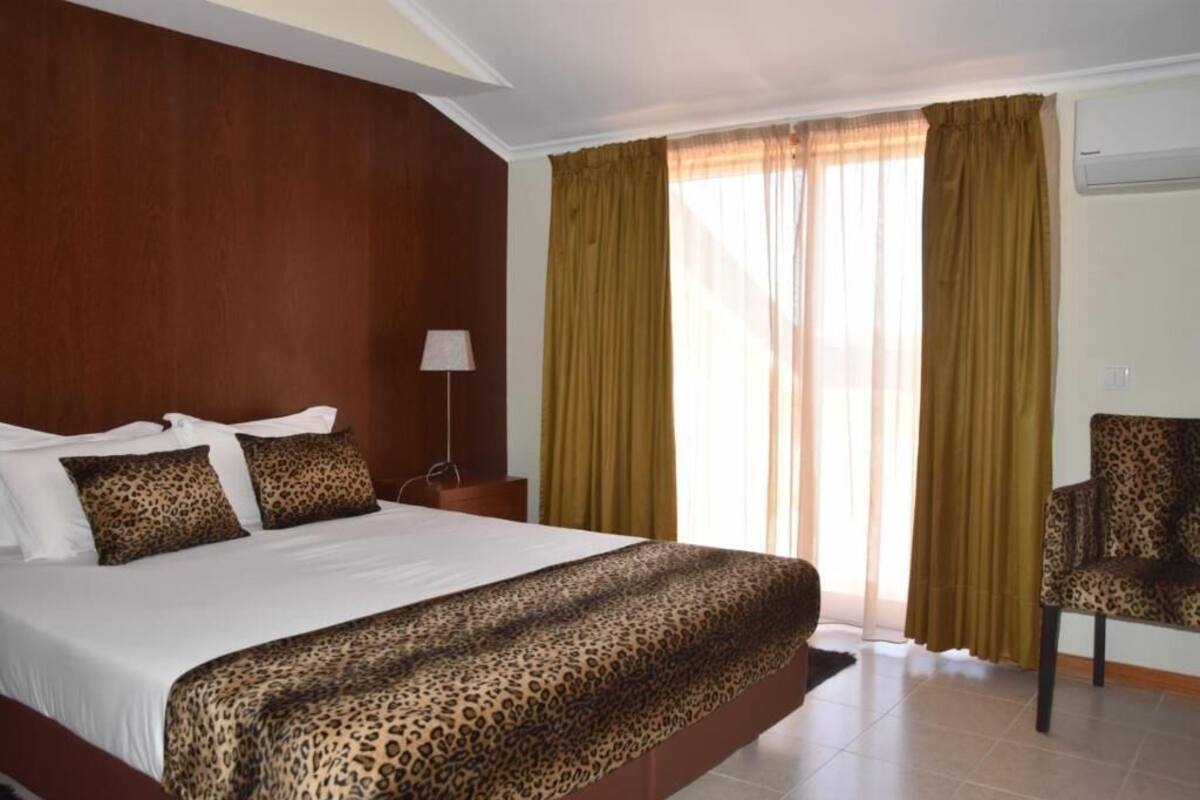 A hotel room with a large bed, a chair, and a window with curtains.