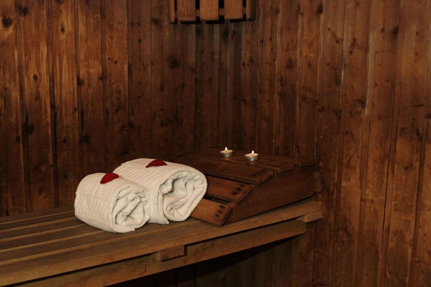 A wooden room with a bench, two rolled towels, and three lit candles.