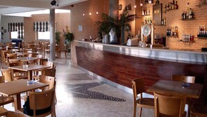 Restaurante com parede de tijolos, mesas e cadeiras de madeira. Há um balcão de bar com garrafas e uma planta.