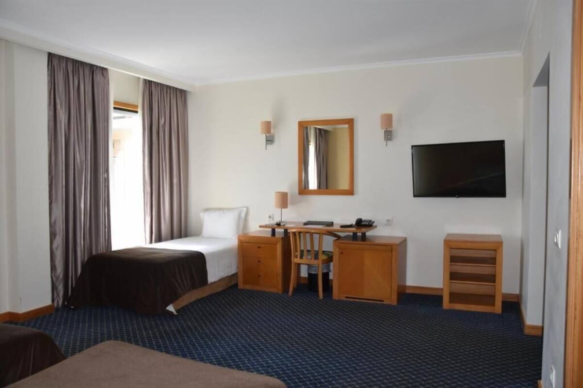 A hotel room with a bed, desk, chair, TV, and a small cabinet.