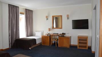 Habitación de hotel con cama, escritorio, silla, televisor y un mueble pequeño.