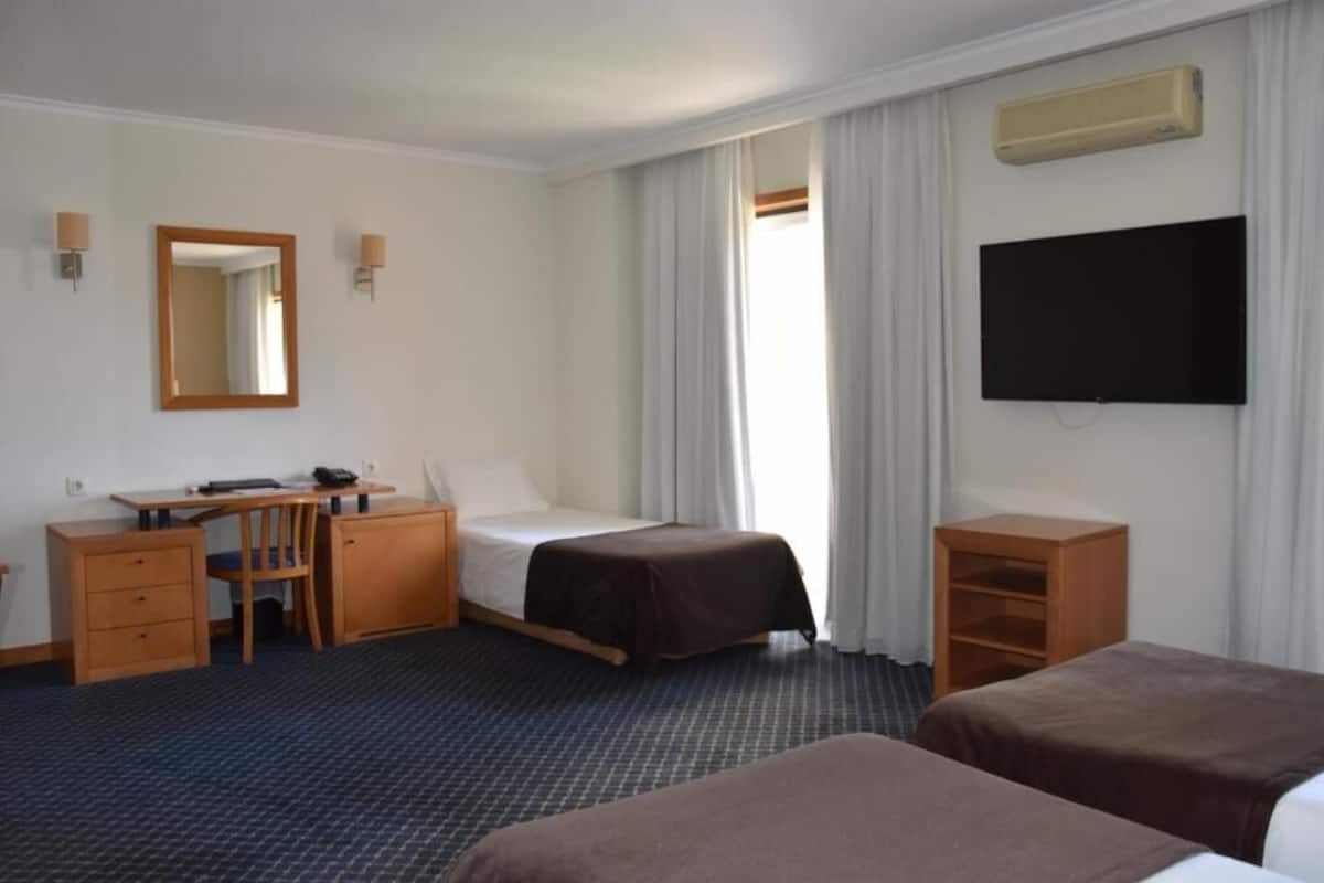 A hotel room with a bed, a desk with a chair, a TV, and a small cabinet.