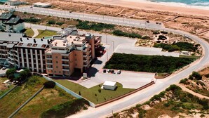 Vista aérea de um hotel à beira-mar com vários edifícios, uma estrada curva e uma praia ao fundo.