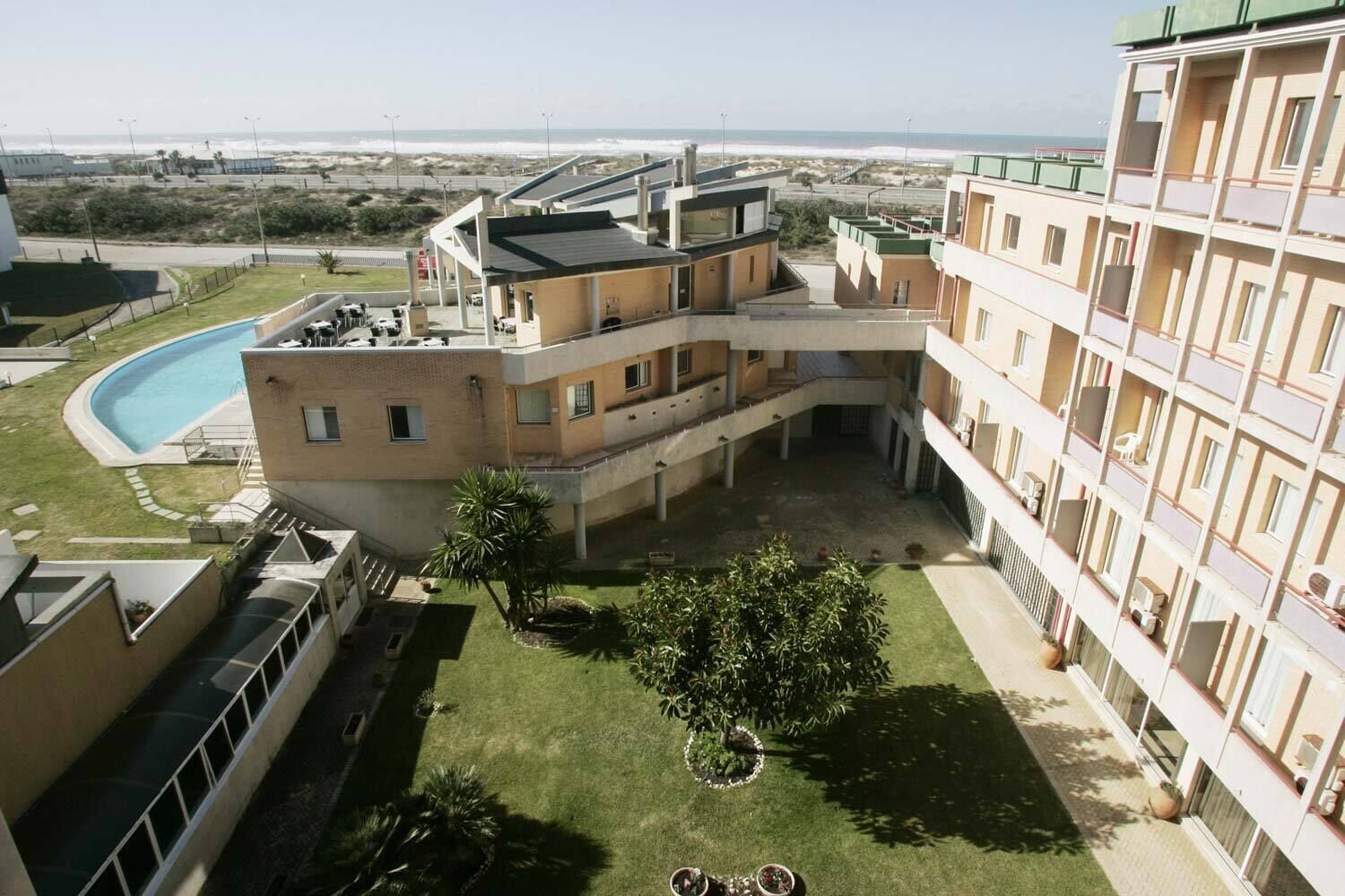 Un hotel a più piani con piscina, area salotto esterna e vista sulla spiaggia.