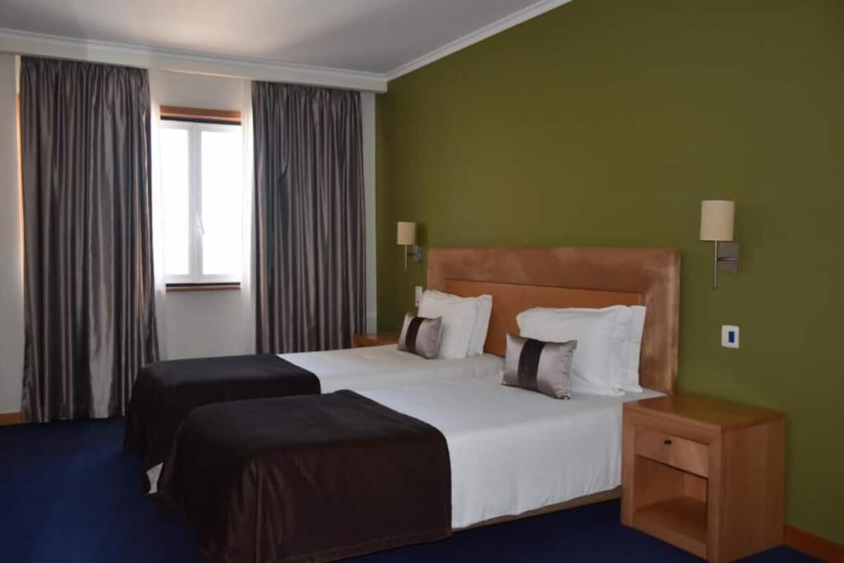 A hotel room with two beds, a wooden headboard, two bedside lamps, and a window with curtains.