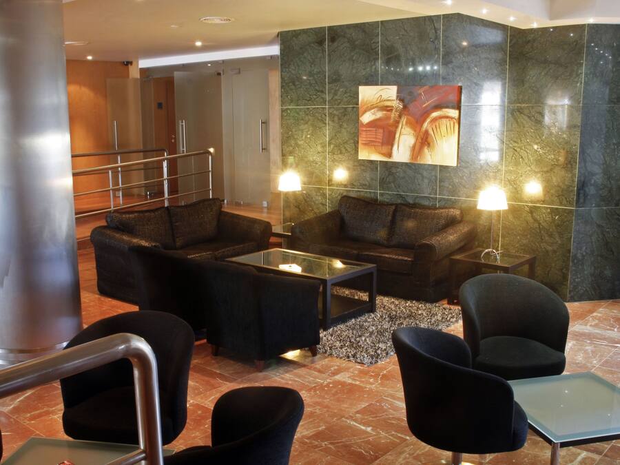 Un hall con zona de estar que incluye sofás y sillones, una mesa de centro de vidrio y un cuadro colgado en la pared.
