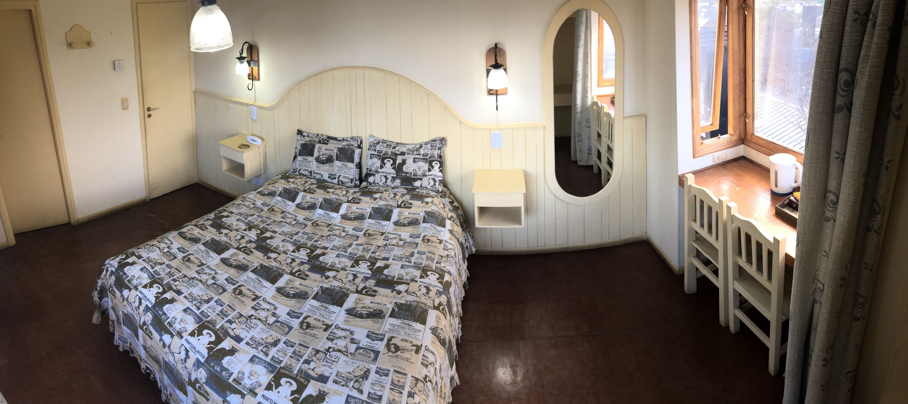 Une chambre à coucher comprenant un lit, des lampes de chevet, un miroir, une fenêtre avec des rideaux et une petite table avec une chaise.