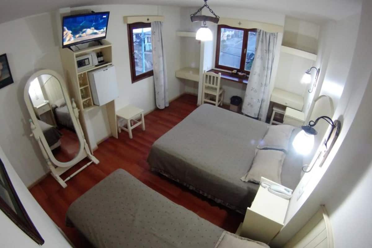 A compact bedroom with a bed, a desk, a chair, a television, and a window.