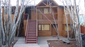 Una cabaña de madera con una escalera central, rodeada de árboles.