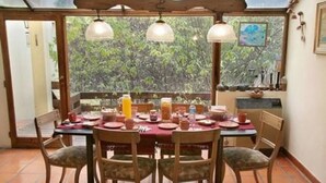 Comedor con mesa dispuesta para cuatro personas, sillas alrededor y vista a zonas verdes a través de amplios ventanales.