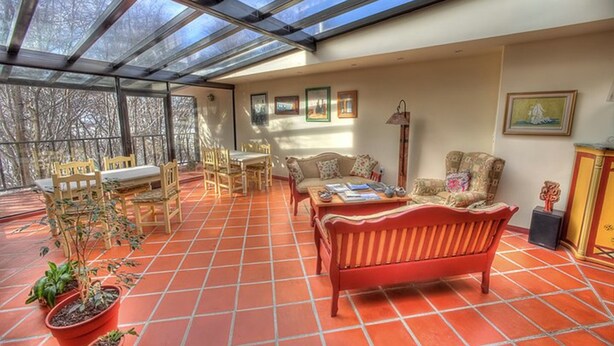 Una habitación soleada con techo de vidrio, muebles de madera y plantas en macetas.