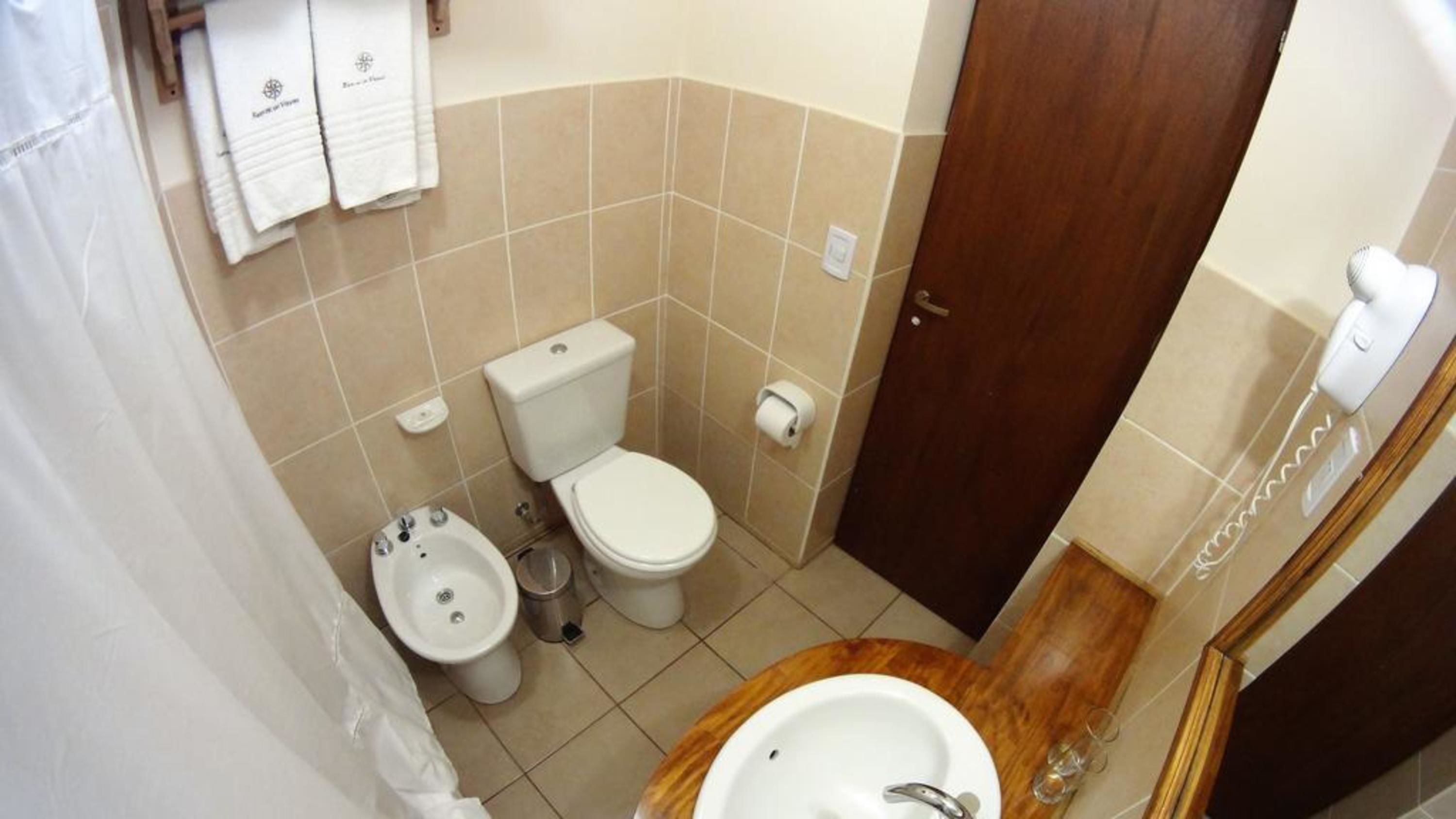 Ein kleines Badezimmer mit Toilette, Bidet und Waschbecken. Handtücher hängen an der Wand und es gibt einen Holztisch für Kosmetikartikel.