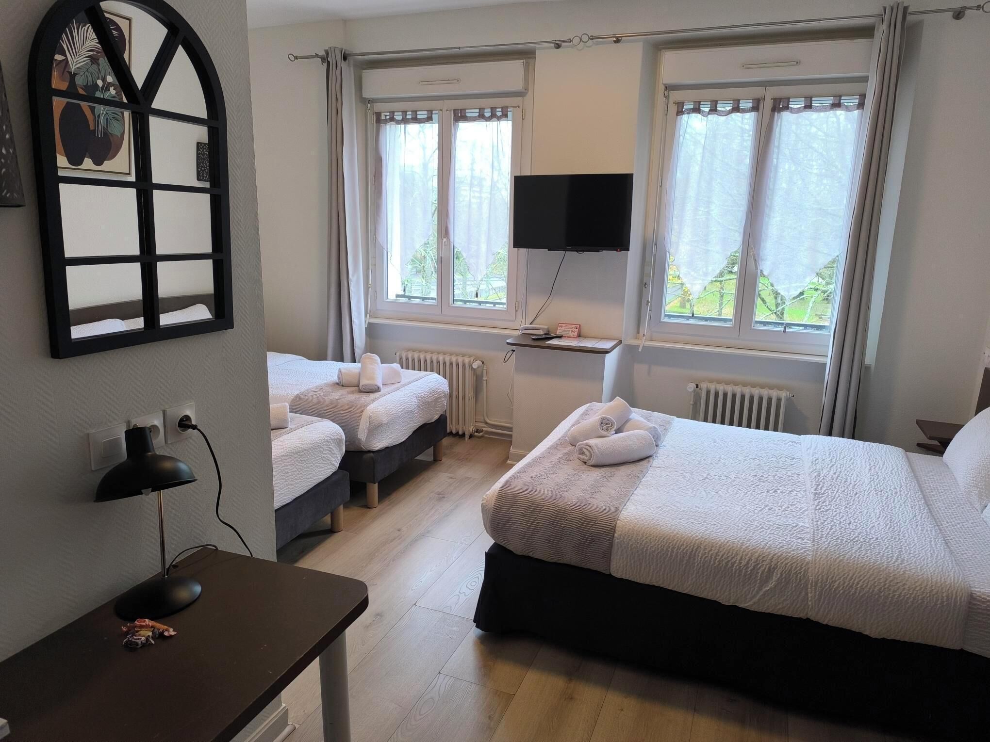 Camera d'hotel con due letti, una scrivania con un computer, una televisione e una finestra con tende.