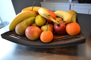 A fruit bowl containing bananas, pears, apples, and oranges on a dark plate. - Agena (Brest)