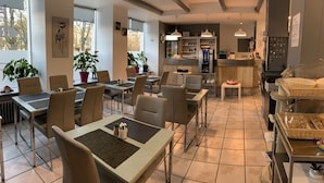 A spacious dining area with multiple tables and chairs, a kitchen area with a refrigerator and counter, and potted plants.