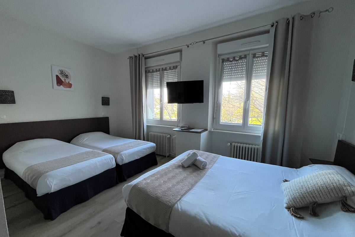 A hotel room with two single beds, a larger bed, a flat-screen TV, and a window with curtains.