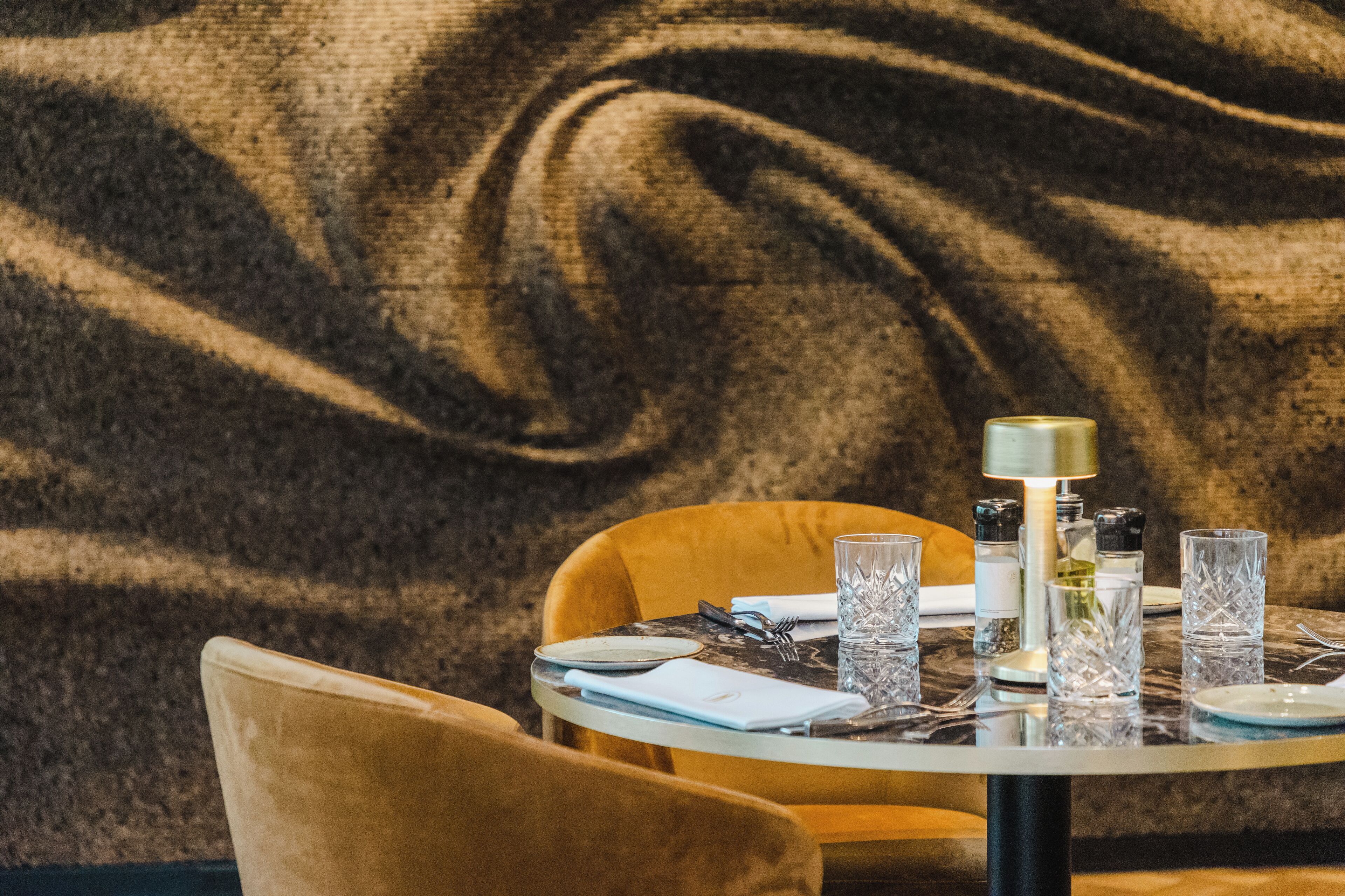 A dining table set with plates, glasses, and cutlery, with a textured wall in the background.