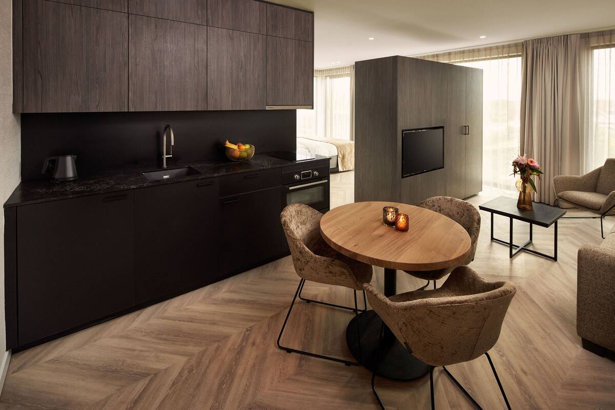 A modern kitchen with dark cabinetry, a built-in oven, and a dining area with a round wooden table and two chairs.