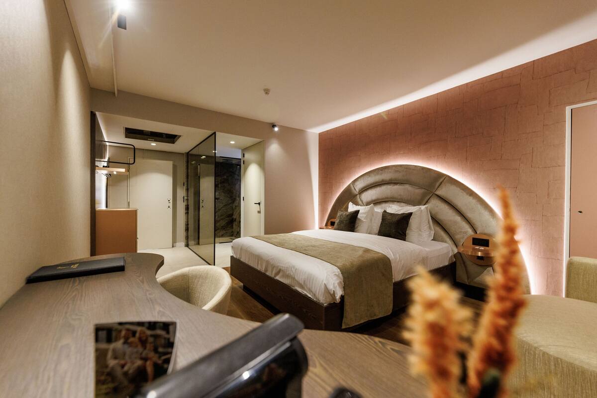 A modern hotel room with a bed, a desk, a chair, and a mirror.