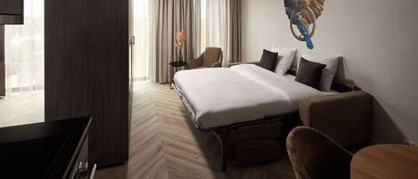 A hotel room with a large bed, a desk, a chair, and a wall-mounted artwork.