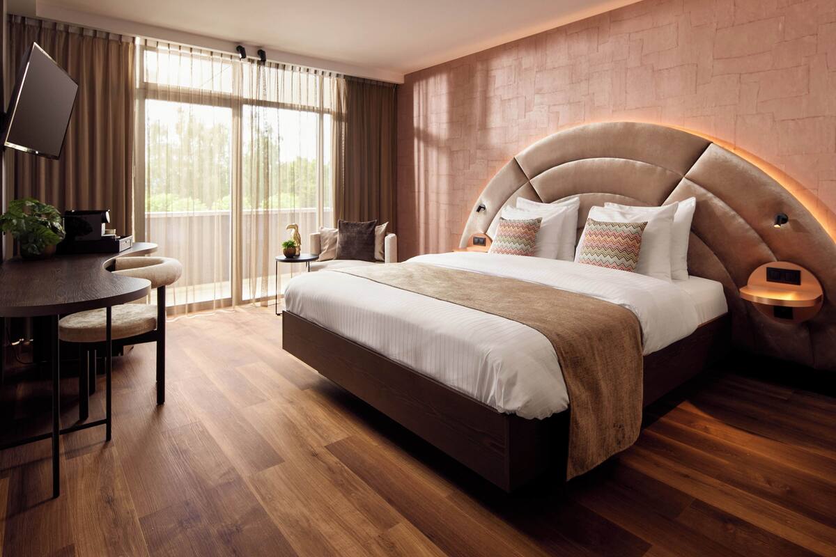 A modern bedroom with a large bed, a desk, and a TV.