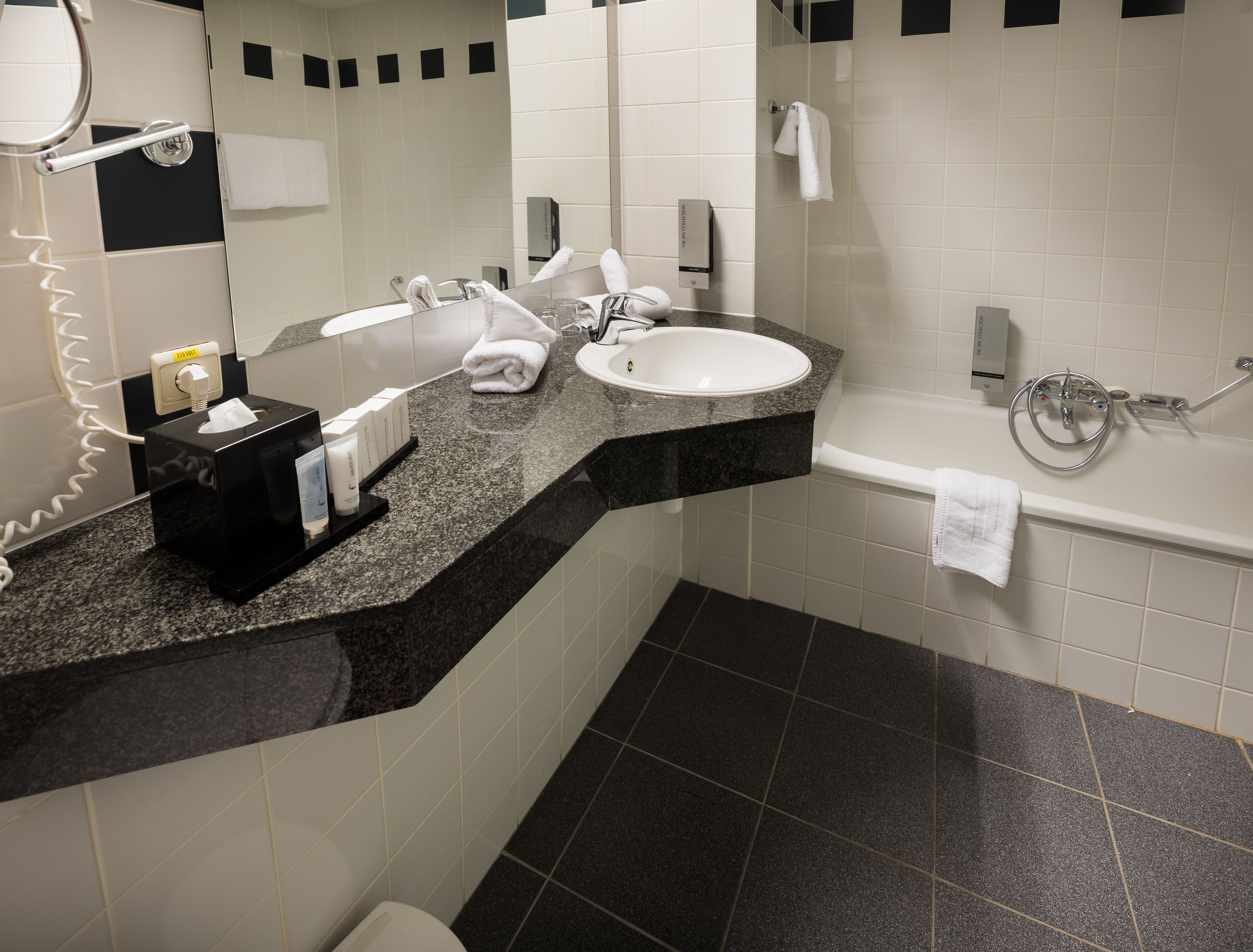 Een moderne badkamer met een granieten aanrechtblad, een wit wastafelmeubel en een bad.