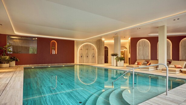 A modern indoor swimming pool with a clear view of the pool, steps leading into the water, and a seating area with cushions. - Van Der Valk Hotel Beveren (Beveren)