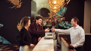A bar area with a long counter, a cash register, and a barista. There are chairs and a table in the background. - Van Der Valk Hotel Beveren (Beveren)