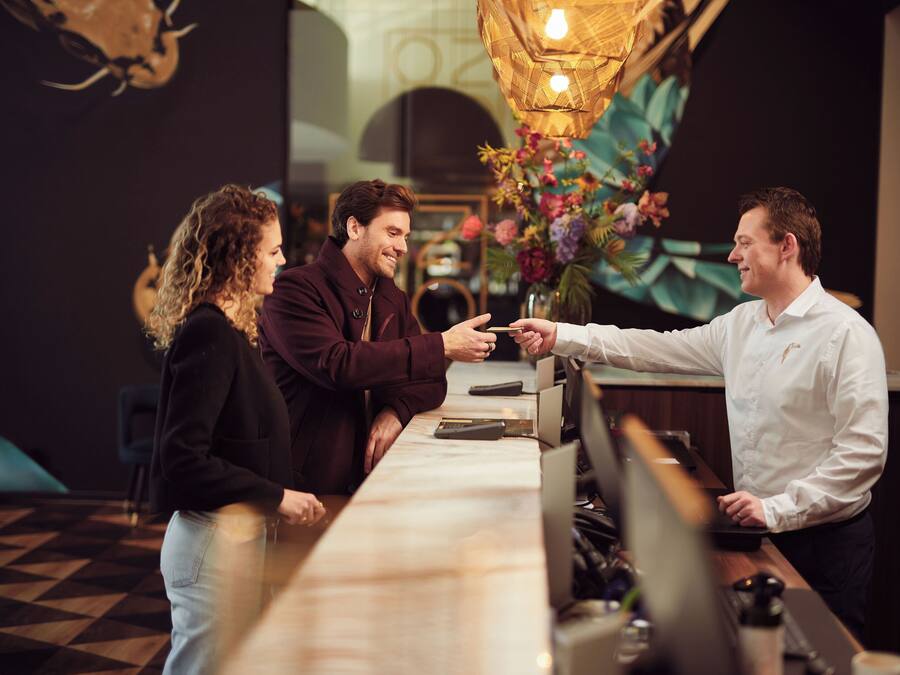 A bar area with a long counter, a cash register, and a barista. There are chairs and a table in the background.