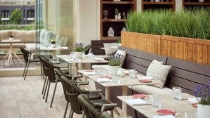 A restaurant with outdoor seating, wooden tables, wicker chairs, and a planter with greenery. - Van Der Valk Hotel Beveren (Beveren)