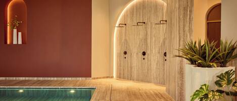 A modern indoor pool area with a wooden floor, a large wall with a wooden panel design, and a small window with a plant.