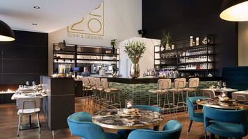 A modern restaurant interior with a sushi bar, bar seating, and a variety of dining tables and chairs.
