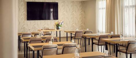 A conference room with tables, chairs, a large screen, and a decorative vase.