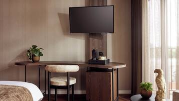 Habitación de hotel con cama, escritorio, silla, televisor, cafetera y planta en maceta.