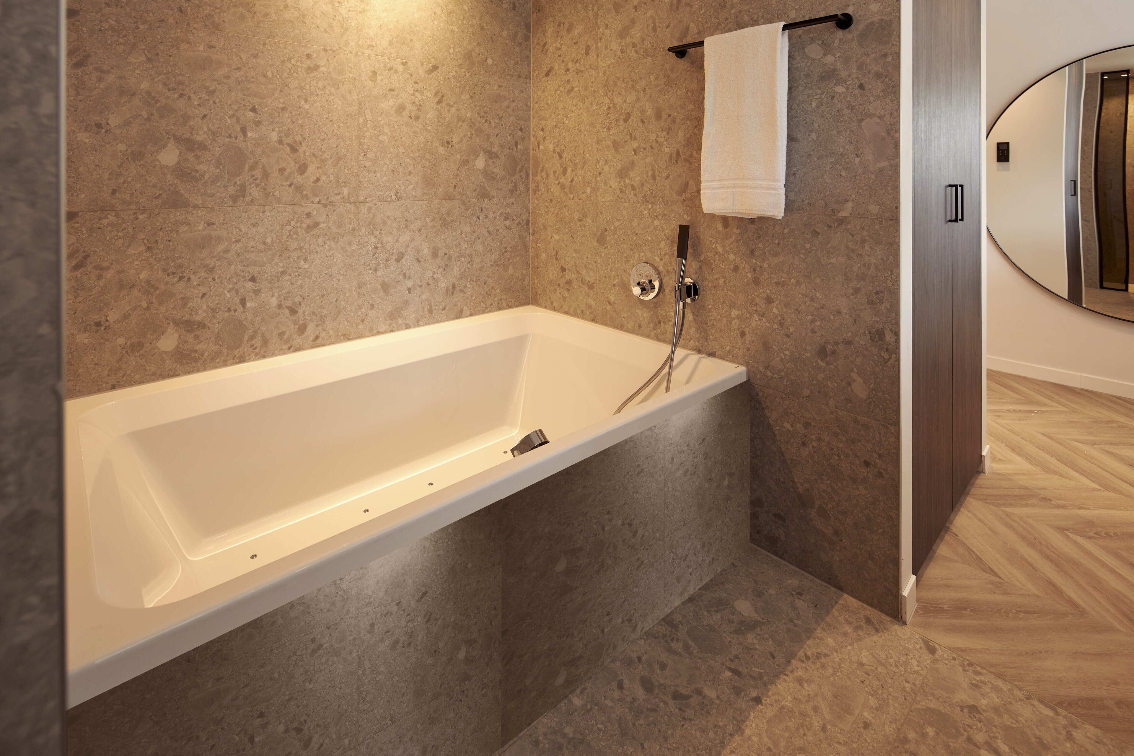 A modern bathroom with a freestanding bathtub, a towel rack, and a wooden floor.